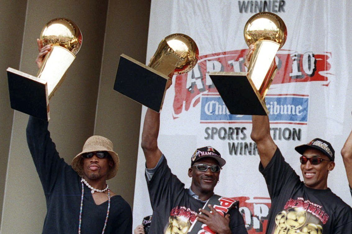 Dennis Rodman, Michael Jordan y Scottie Pippen muestran 3 trofeos del campeonato de la NBA 1997.